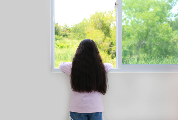 Caucasian little kid girl lies at window of house and watching out. Back view. - Fotó, kép