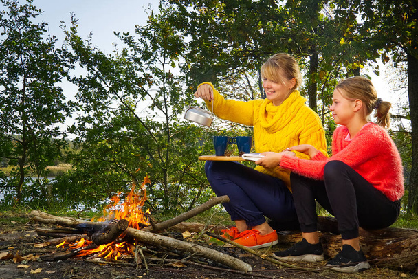 mom and daughter making fire in woods. mother and daughter in the autumn forest sitting by the fire. - Foto, Imagen