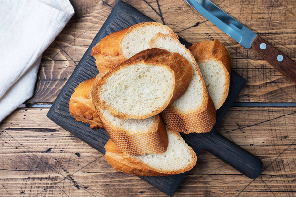 Fresh white bread baguette cut slays on a wooden cutting Board. - Фото, изображение