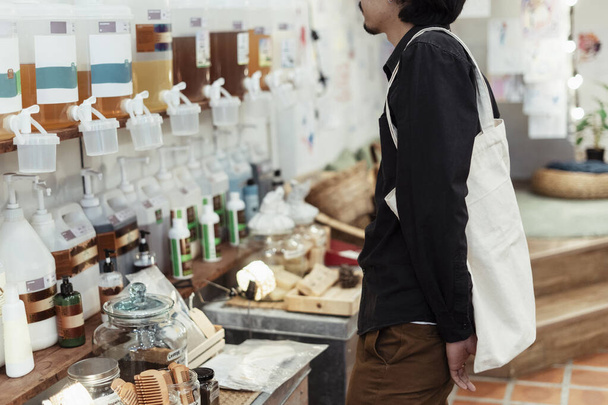 Kręcone czarne włosy facet z torbą płócienną patrząc na produkt w sklepie. - Zdjęcie, obraz