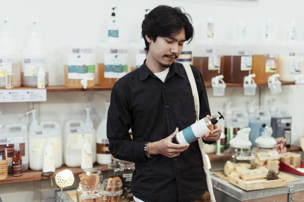 Asian man choosing local product in eco shop. - Фото, изображение