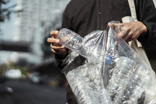 Das abgeschnittene Bild einer Plastikflasche sammelt der Mann im schwarzen Hemd in der Stadt. - Foto, Bild