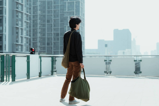Černé vlasy muž stojící na terase stanice mrakodrap při pohledu na obklopený mrakodrap. - Fotografie, Obrázek