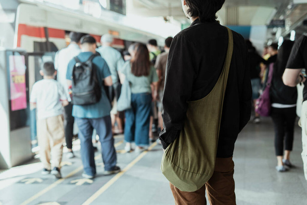 Ein Mann in schwarzem Hemd steht am Skytrain-Bahnhof und betrachtet die Menschen in der Schlange. - Foto, Bild