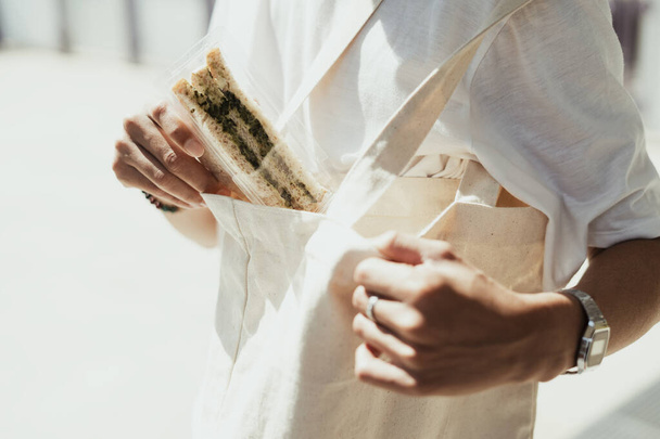 Immagine ritagliata di sandwich vegetariano che l'uomo prende dalla sua borsa di tela bianca. - Foto, immagini