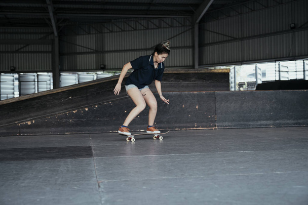 Dark blue polo shirt woman try to balance herself on longboard with wide legs. - 写真・画像