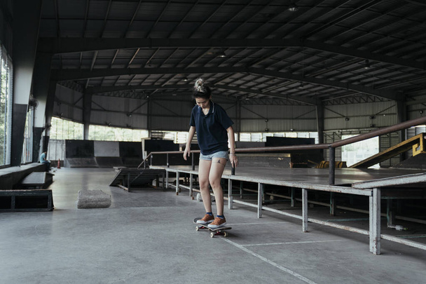 vrouw in donker blauw polo shirt schuif longboard onder haar voeten tijdens het spelen in de vrije tijd in skateboard veld. - Foto, afbeelding