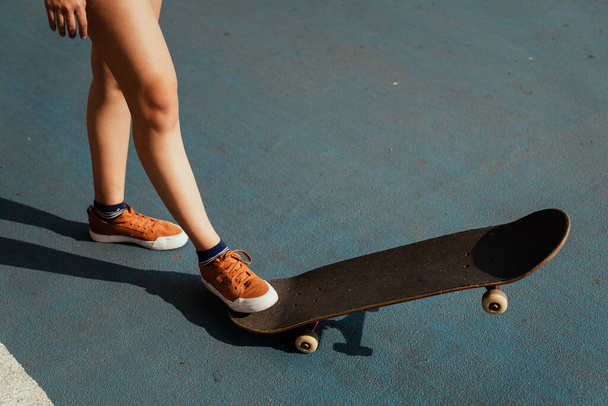 Imagen recortada de las piernas de la mujer mientras juega longboard en la parte azul con un lado hacia abajo y un lado hacia arriba. - Foto, Imagen