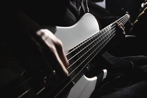 Крупним планом вид на п'яти струнну бас-гітару і руки музиканта, освітлені контрастним світлом в темній кімнаті
. - Фото, зображення
