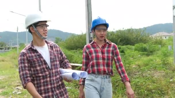 Langzame beelden van het controleren van de bouwplaats, Aziatische ingenieurs in helmen lopen rond de bouwplaats en controleren met blauwdrukken - Video