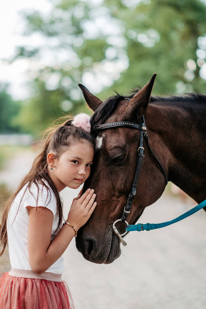 Η φιλία ενός παιδιού με ένα άλογο. Ένα κοριτσάκι χαϊδεύει στοργικά το άλογό της. Περπάτημα κορίτσια με ένα άλογο στο πάρκο το φθινόπωρο. - Φωτογραφία, εικόνα