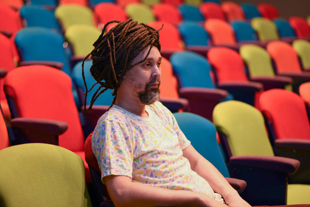 Una persona seduta da sola in teatro con sedie colorate luminose - Foto, immagini