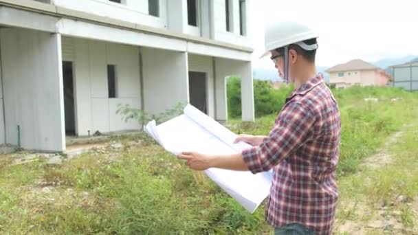 Lassú felvételek az építési terület ellenőrzéséről, ázsiai mérnökök sisakokban sétálnak az építkezésen és tervrajzokkal ellenőrzik - Felvétel, videó