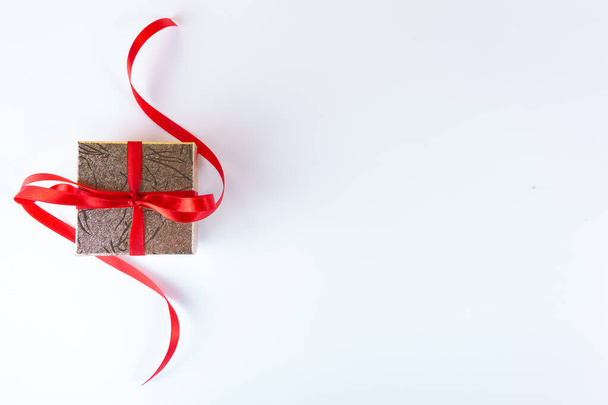 gold gift with red ribbon on a light background with copy space. - Foto, afbeelding