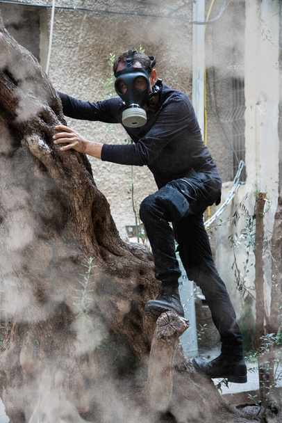 環境災害。ガスマスクで黙示録的な生存者を投稿します。煙に囲まれながら木に登るガスマスクの男. - 写真・画像