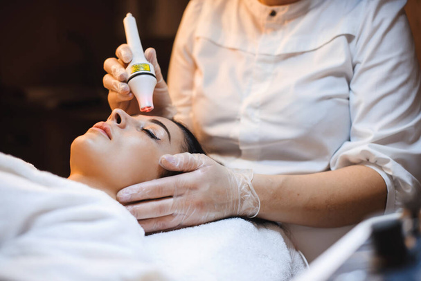 Leugenaar brunette vrouw met gezichtsbehandeling procedures in spa salon met behulp van moderne apparatuur - Foto, afbeelding
