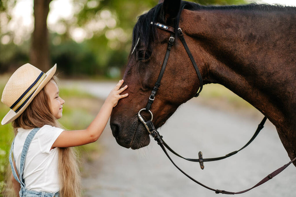 Vriendschap van een kind met een paard. Een klein meisje streelt liefdevol haar paard. Wandelende meisjes met een paard in het park in de herfst. - Foto, afbeelding
