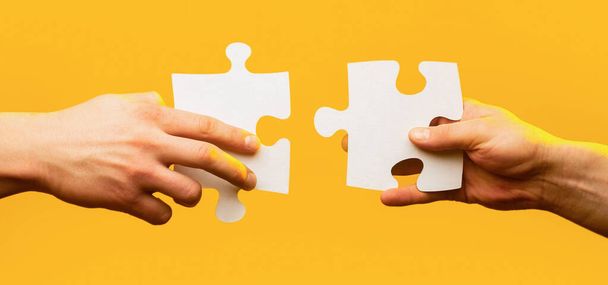 Two hands trying to connect couple puzzle piece on yellow background. Teamwork concept. Holding puzzle. Closeup hand of connecting jigsaw puzzle. Business solutions, success and strategy concept - Foto, Imagen