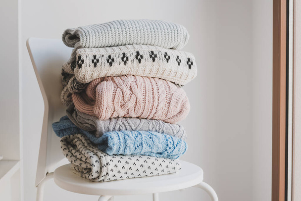Pile of warm sweaters on white chair. Woolen knitwear clothes for autumn and winter season. Handmade jumpers - Photo, image