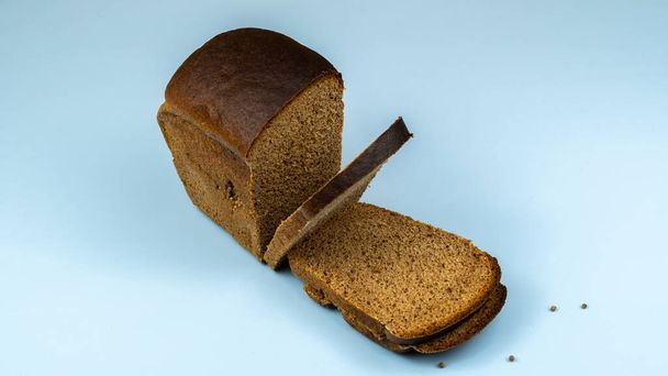 Полубуханка ржаного хлеба и нарезанный, крупным планом на синем фоне - Фото, изображение