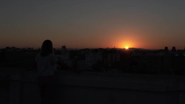 Девушка смотрит на закат на крыше дома - Кадры, видео