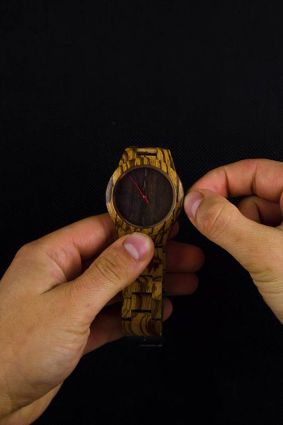 Un homme étire une montre-bracelet et ajuste l'heure sur fond noir. - Photo, image