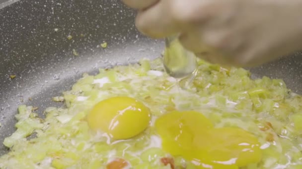Video in Zeitlupe, in dem Hühnereier in eine Pfanne mit Zwiebeln, Gewürzen und Gewürzen zerkleinert werden. Rührei, Frittata, Omelette oder Spiegeleier kochen. Zubereitung von Diätspeisen, richtige vegane Ernährung - Filmmaterial, Video