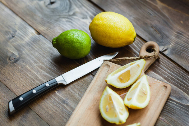 Board with lemon and lime for slicing, preparing for cooking, salads and appetizers, lemon juice, decorating dishes, cook, man cutting a lemon, holding a kitchen knife in his hand, cutting a lime - Foto, immagini