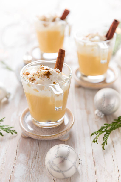 Eggnog with cinnamon and nutmeg for Christmas and winter holidays. With Xmas decorations on wooden background. - Fotografie, Obrázek