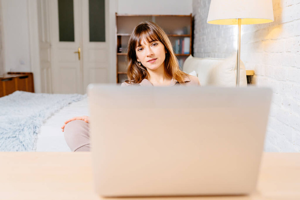 Зрелая брюнетка успешная деловая женщина смотрит в камеру во время работы с ноутбуком на домашнем интерьере в офисном рабочем пространстве. - Фото, изображение