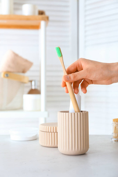 Женщина берет зубную щетку из чашки в ванной комнате - Фото, изображение