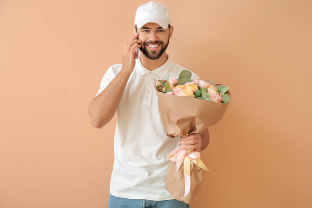 Delivery man with bouquet of flowers talking by phone on color background - Foto, imagen