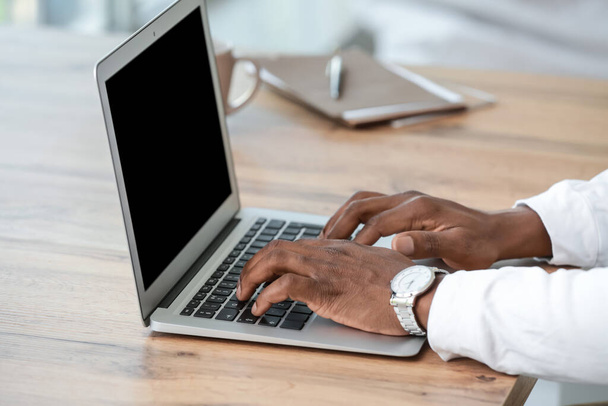 Афроамериканец, работающий на ноутбуке в офисе, крупным планом - Фото, изображение