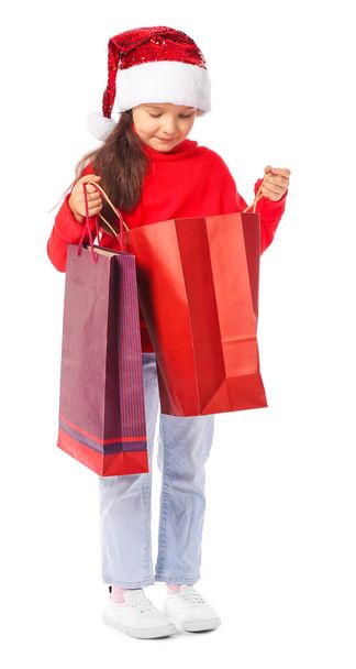 Cute little girl in Santa hat and with shopping bags on white background - 写真・画像