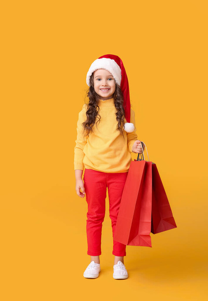Nettes kleines Mädchen mit Weihnachtsmütze und mit Einkaufstaschen auf farbigem Hintergrund - Foto, Bild