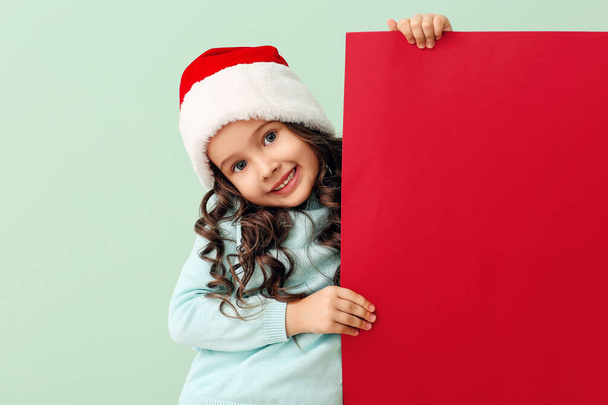Linda niña en el sombrero de Santa y con cartel en el fondo de color - Foto, Imagen