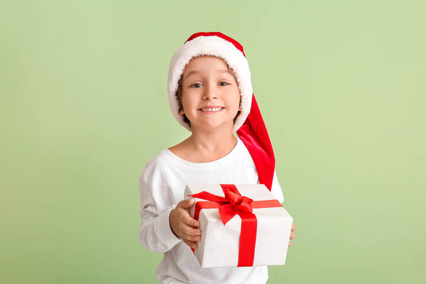 Cute little boy in Santa hat and with gift on color background - Foto, imagen