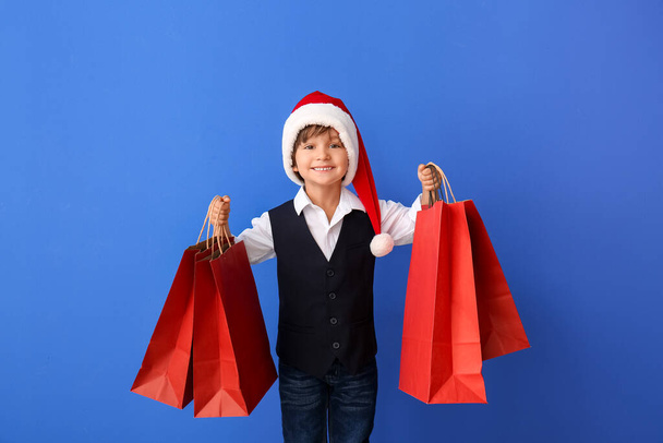 Roztomilý chlapeček v klobouku Santa a s nákupními taškami na barevném pozadí - Fotografie, Obrázek