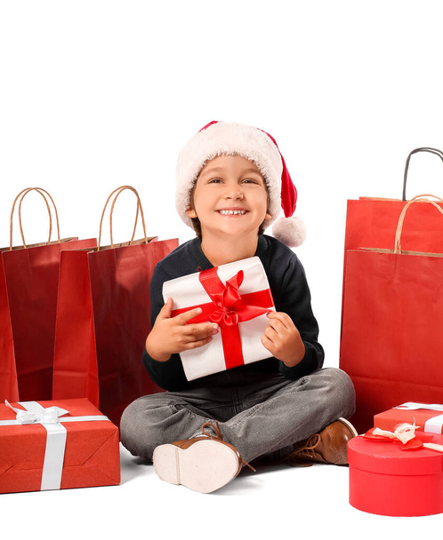 Leuke kleine jongen in Santa hoed, met geschenkdozen en boodschappentassen op witte achtergrond - Foto, afbeelding