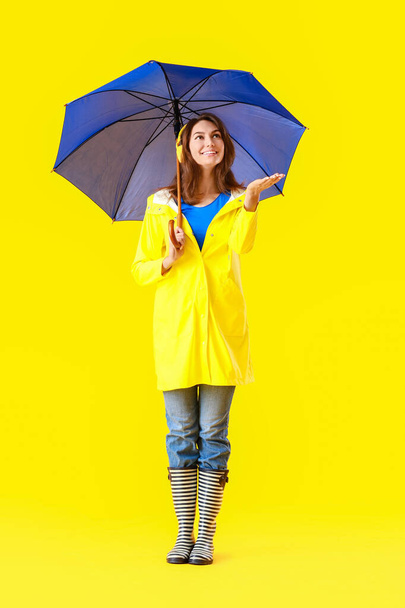 Beautiful young woman in raincoat and with umbrella on color background - Photo, Image