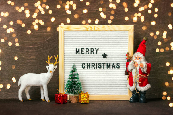 Beyaz geyik, Noel Baba, ışıklar, ağaç, hediye kutusu. Koyu ahşap arka planda Mutlu Noeller Noel kartı konsepti.. - Fotoğraf, Görsel