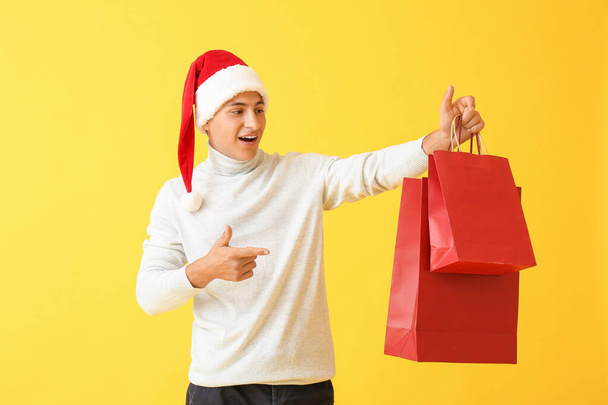 Schöner Mann mit Weihnachtsmütze und Einkaufstaschen auf farbigem Hintergrund - Foto, Bild