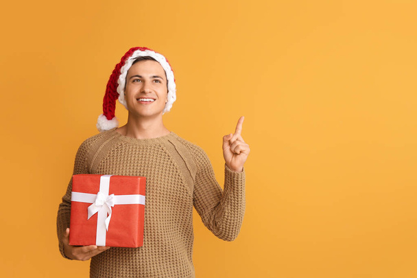 Handsome man in Santa hat and with gift pointing at something on color background - Fotoğraf, Görsel