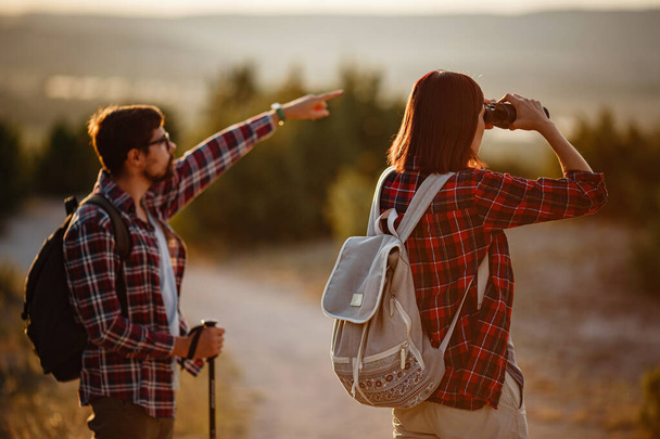 Portrait de jeune couple heureux s'amusant lors de leur voyage de randonnée. Couple de randonneurs caucasiens et asiatiques s'amusant en vacances d'été. Ils observent la nature avec des jumelles. - Photo, image