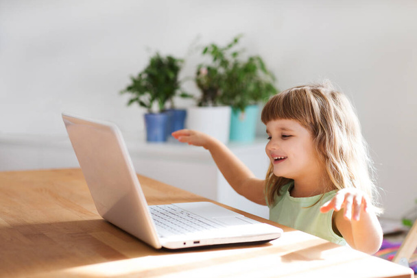 Child girl is using a laptop and communicates on the Internet at home. Training online. quarantine. Corona Virus. kid study at home. - Фото, зображення