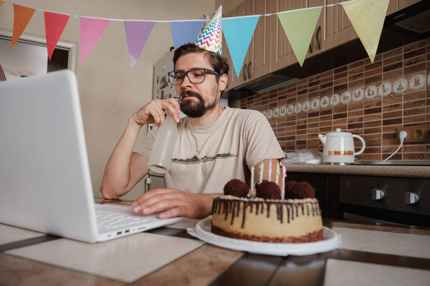 Férfi ünnepli születésnapját online karantén idő. Egy srác, aki a szülinapját videóhívással ünnepli virtuális partin a barátaival. Coronavirus járvány 2020. - Fotó, kép