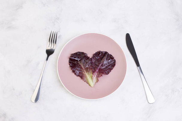 Verse hartvormige sla bladeren op een bord met een vork en mes. Ecologisch concept. Gezond vegetarisch voedsel. - Foto, afbeelding