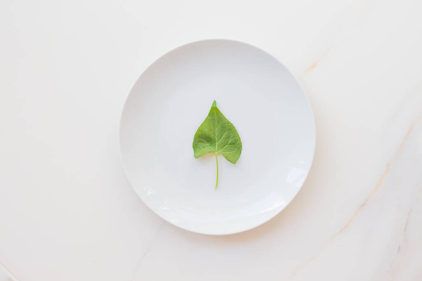 The concept of diet and weight loss, fasting and cleansing the body. Empty white plate on a white marble table. Detox the body with green foods. - Fotoğraf, Görsel
