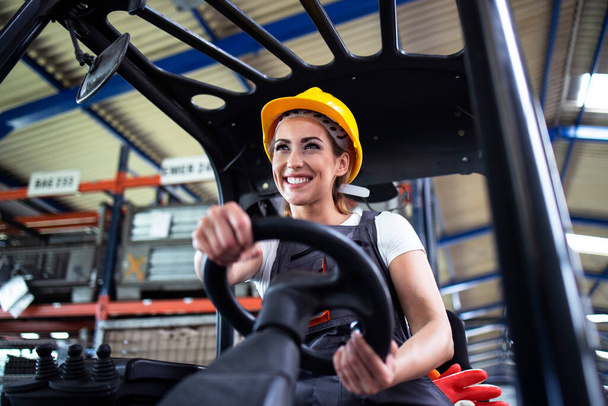Professional female industrial driver operating forklift machine in factory's warehouse. - Photo, Image