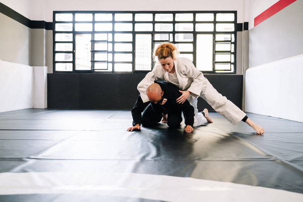 Drei Partner eines Kampfsporttrainings wie Judo oder Karate mit Kimonos, die Techniken auf der Turnmatte üben, tragen aufgrund der Covid 19 Coronavirus-Pandemie Gesichtsmasken. - Foto, Bild